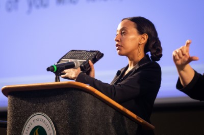 [Image description: Haben Girma holds up her digital braille device while speaking to students at Sacremento State]