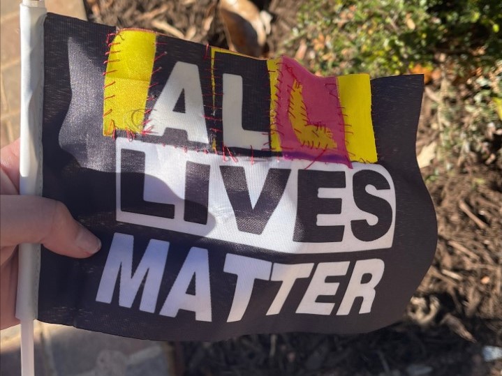 The  word All stitched to replace the word Black on a Black Lives Matter flag.