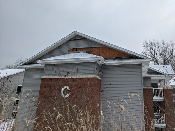 Siding missing from the front of North Village C. In the middle, the attic space is slightly exposed. Soffit is also damaged.